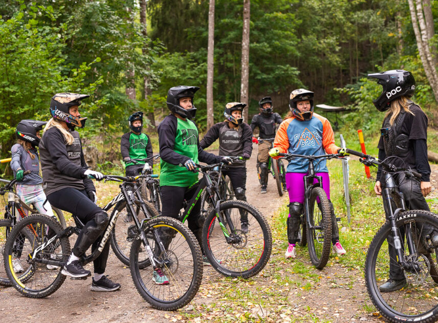 En grupp kvinnor med cyklar och instruktör sedda från sidan, de är omgivna av skog.