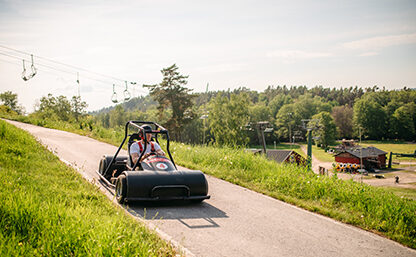 Bild på en av Flottbros Downhill bilar som susar ner för backen, gräset är grönt och solen skiner.