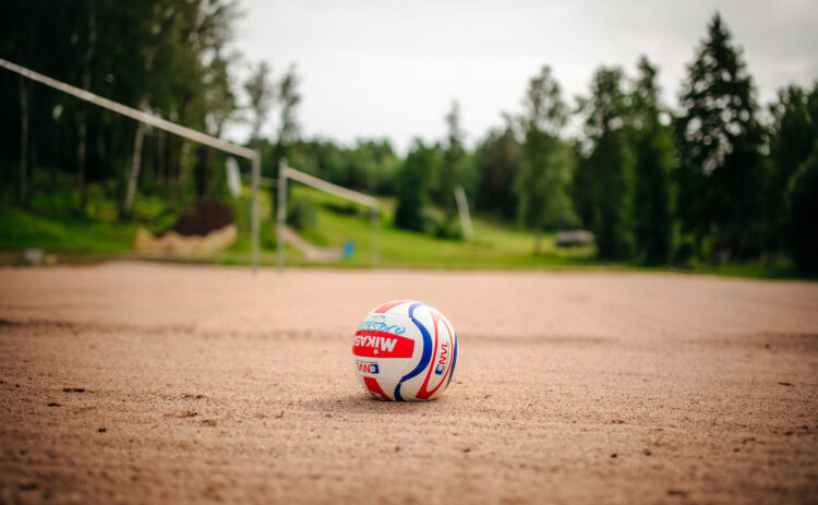 En beachvolleyboll ligger på en sandstrand i bakgrunden syns grön skog och blå himmel.