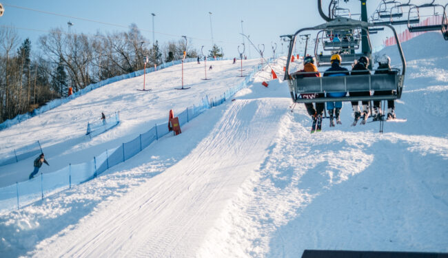 I bilden syns ryggarna på fyra personer som åker upp för Flottsbrobackens stolslift en solig vinterdag.