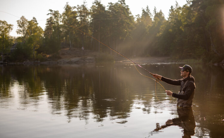 Bild på en man sedd från sidan som kastar med flugspö ute i en sjö.