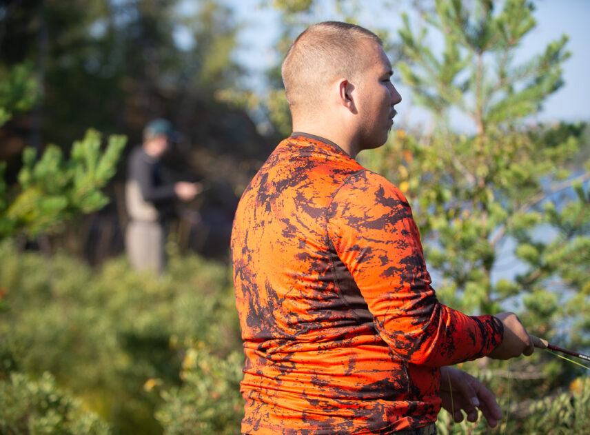 Närbild på en person sedd från sidan som hållerett fiskespö, i bakgrunden syns ytterligare en person som fiskar.