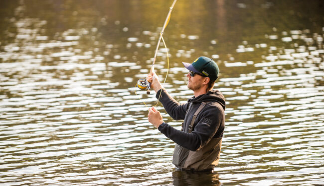 Bild på en person som står i vattnet och fiskar med flugspö.