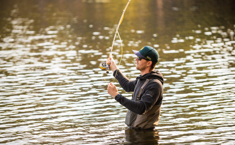 Bild på en person som står i vattnet och fiskar med flugspö.