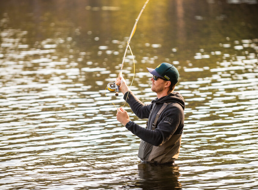 Bild på en person som står i vattnet och fiskar med flugspö.
