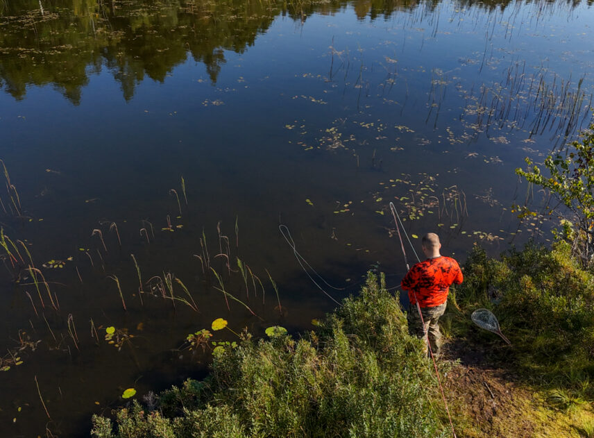 vy på en person som fiskar vid en sjö sedd snett uppifrån.