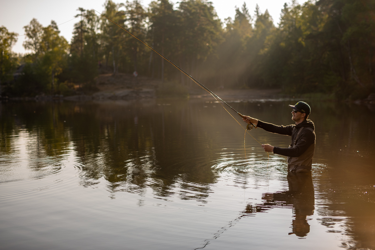 En man står i en sjö och fiskar med ett kastspö.