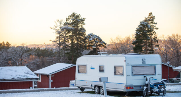Vinterbild på en husvagn som står på campingplatsen, i bakgrunden syns röda stugor.