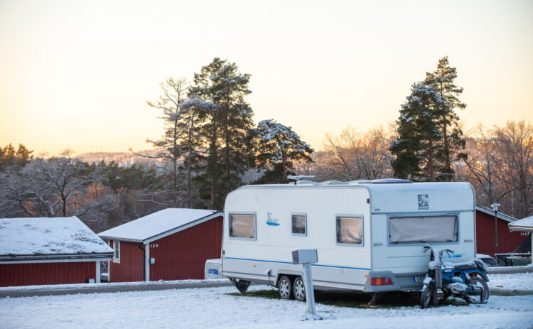Vinterbild på en husvagn som står på campingplatsen, i bakgrunden syns röda stugor.