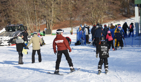 Bild av instruktör på skidskola och en grupp elever sedda bakifrån.