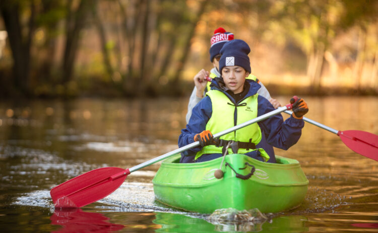 Två ungdomar som paddlar kanot i en kanal.