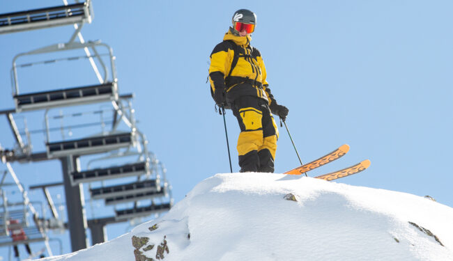 Skidåkare iklädd gul klädsel sett underifrån, i bakgrunden syns blå himmel.