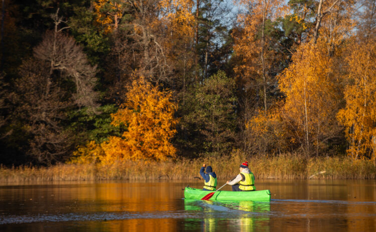 Bilden visar en kanot med 2 personer som paddlar i Albysjön en höstdag, i bakrunden syns lövträd i skiftande höstfärger.