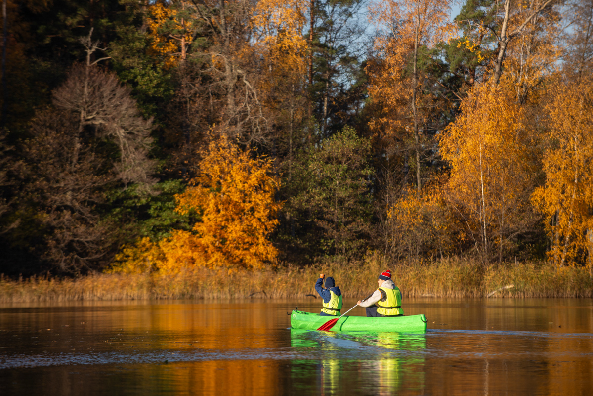 Bilden visar en kanot med 2 personer som paddlar i Albysjön en höstdag, i bakrunden syns lövträd i skiftande höstfärger.