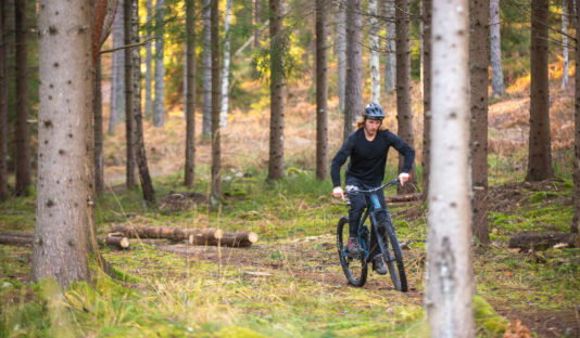 En MTB-cyklist skymtas mellan träden i en skog med blandad vegetation.