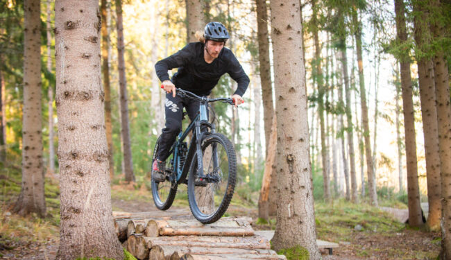 Bild på MTB cyklist som cyklar över stockar i en skog.