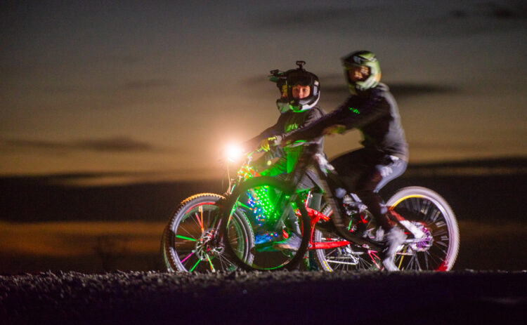 Bild tagen på kvällen på Flottsbro Nightride, cyklister med ljus centralt i bilden, det är mörk bakgrund.