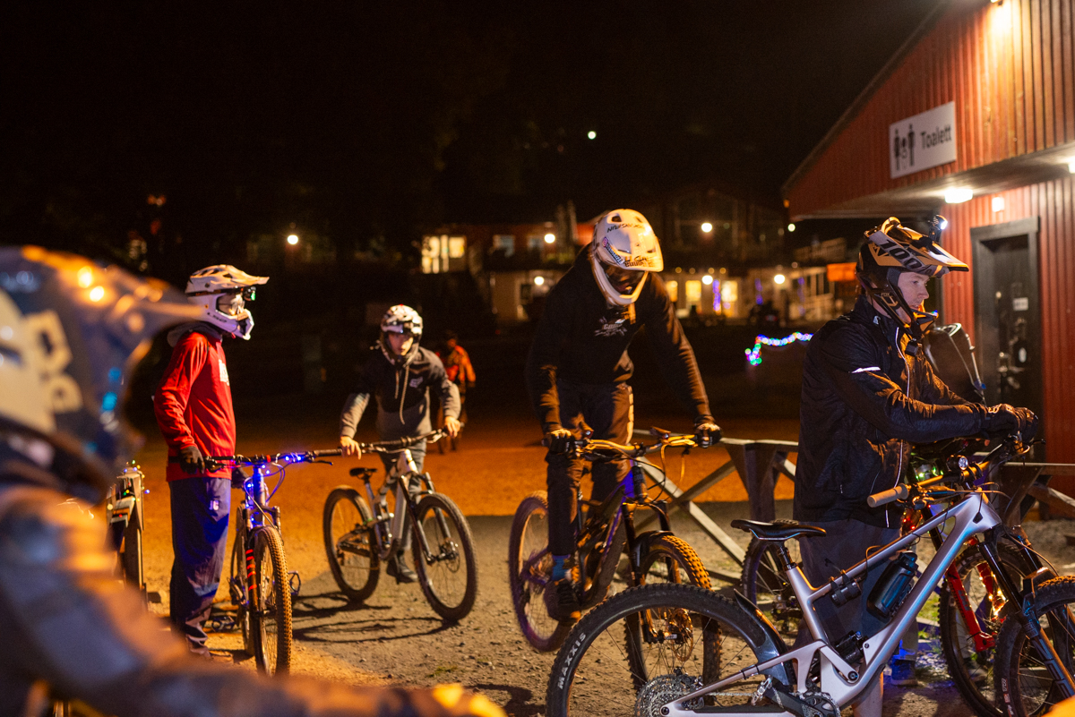 Cyklister i kö till liften i en Bike Park i höstmörker.