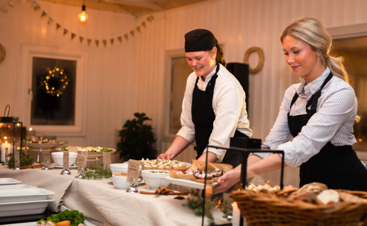 Bild på två unga kvinnor iklädda kockkläder dukar ett julbord.