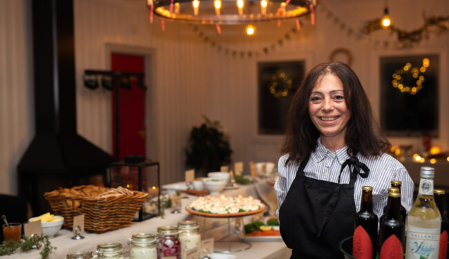 Bild på servitris som håller bricka med drycker framför ett dukat julbord.