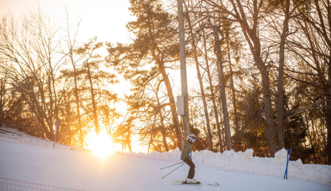 Bild på en skidåkare i solnedgång som åker nedför Flottbros backe, i bakgrunden syns trädtoppar.