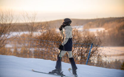 En skidåkare sedd i profil som blickar ut över ett snöigt landskap i skymningen
