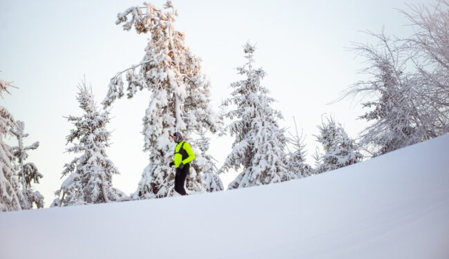 En bild på en man som joggar nedför en vit snöig backe, i bakgrunden syns snöbeklädda granar.