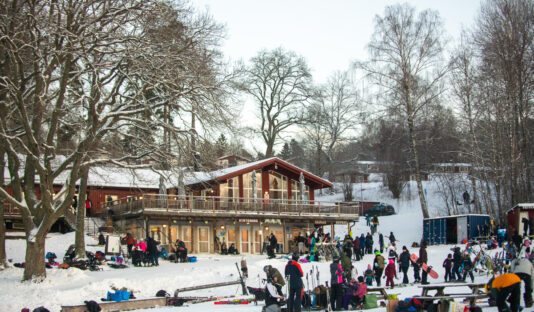 Flottbros värdshus och skidhyra på vintern, i förgrunden syns en grupp människor och skidställ med utrustning.