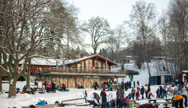 Flottbros värdshus och skidhyra på vintern, i förgrunden syns en grupp människor och skidställ med utrustning.