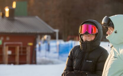 Två skidåkare som talar med varandra sedda i profil, i bakgrunden syns anläggningens lifthus.