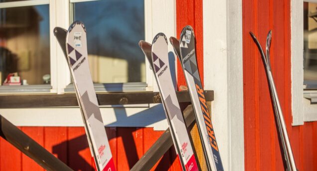 Bild på tre par skidor som lutar mot en röd stugvägg.