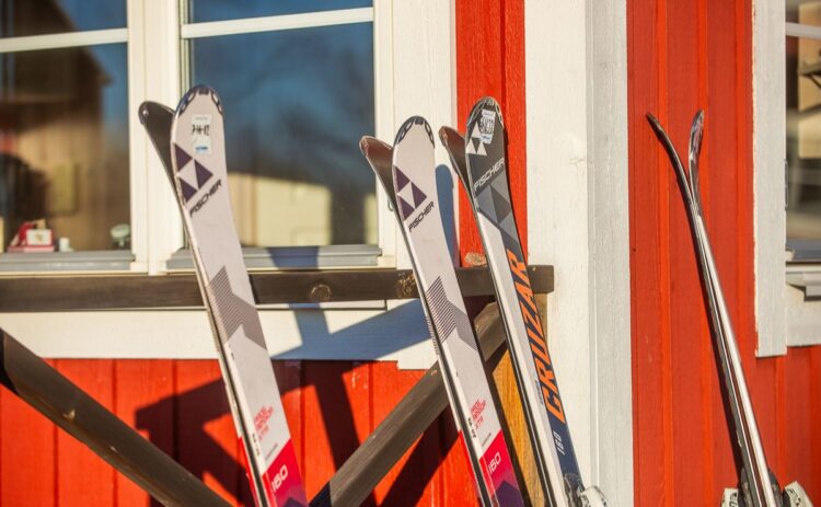 Bild på tre par skidor som lutar mot en röd stugvägg.