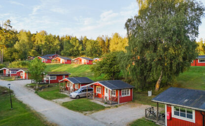 Bilden visar röda en grusväg med röda sommarstugor som ligger på rad, gräsmattor är göra och himlen är blå.