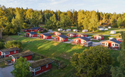 Bilden visar röda en grusväg med röda sommarstugor som ligger på rad, gräsmattor är göra och himlen är blå.