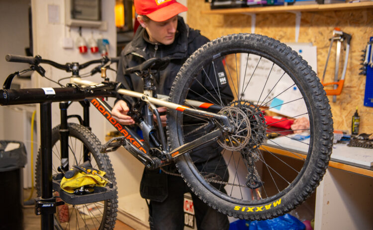 Bild på en cykel och em mekaniker som mekar med den i en verkstad.