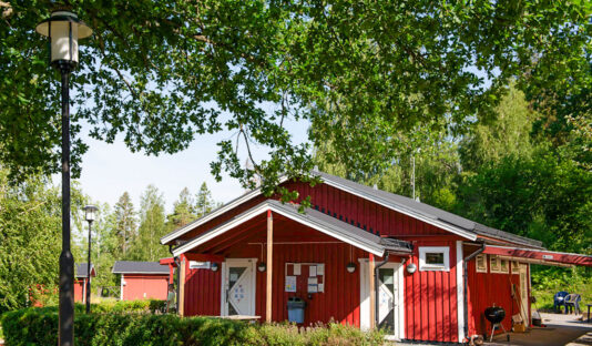 Röd servicebyggnad sedd framifrån omgiven av grönska.