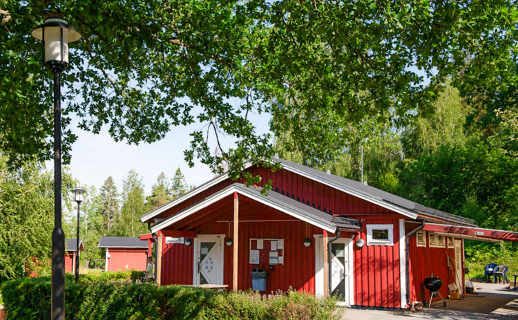 Röd servicebyggnad sedd framifrån omgiven av grönska.