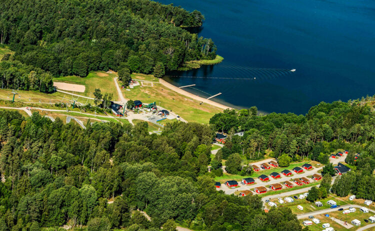 Ett flygfoto på område som visar flottbros backe på sommaren, uppe till höger i bild syns sjön och nedtill syns ett campingområde.