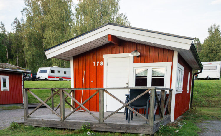 Bild på röd stuga sedd rakt framifrån, i bakgrunden syns två husvagnar.