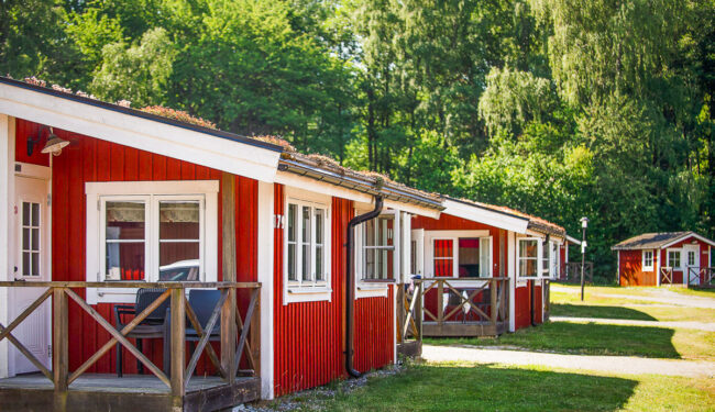 En rad röda stugor på en grön gräsmatta med en lummig grön skog i bakgrunden.