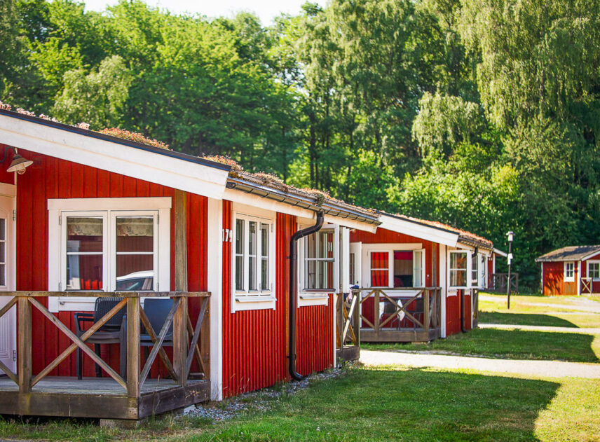 En rad röda stugor på en grön gräsmatta med en lummig grön skog i bakgrunden.