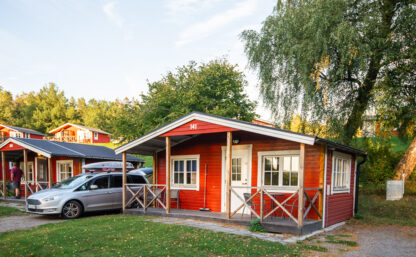 Bild på röd stuga med en parkerad bil sedd från sidan.