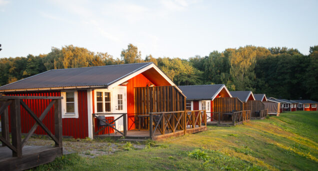 En rad röda stugor på slänten i solnedgången, himlen är blå och i bakgrunden syns grön skog.