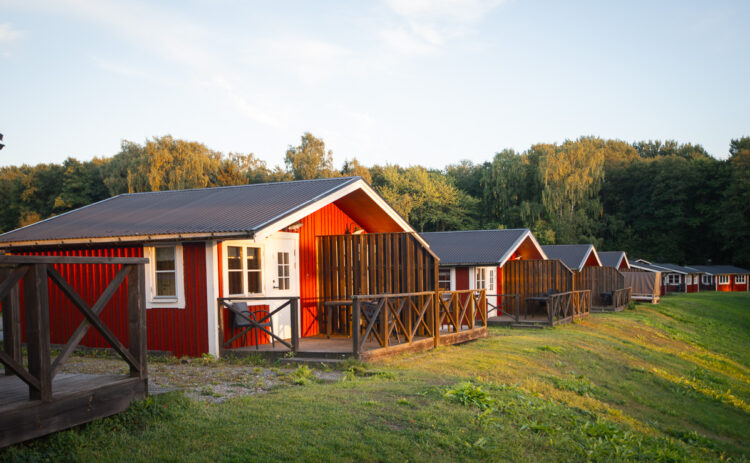 En rad röda stugor på slänten i solnedgången, himlen är blå och i bakgrunden syns grön skog.