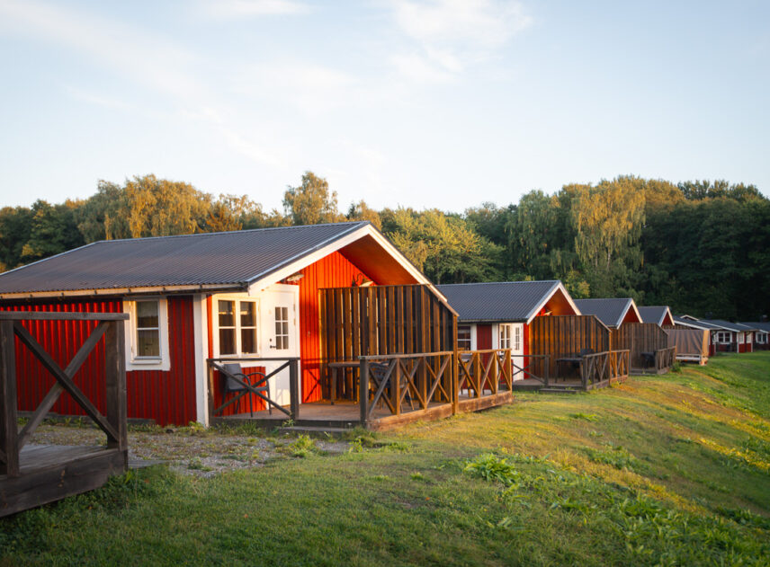En rad röda stugor på slänten i solnedgången, himlen är blå och i bakgrunden syns grön skog.