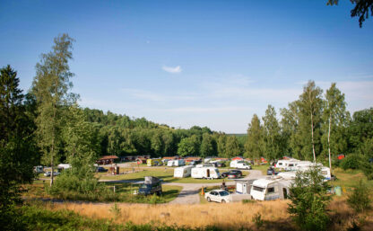 Husvagnar och bilar omgivna av skog, himlen är blå.