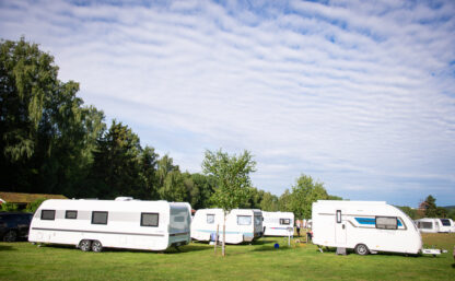 Bilden visar tre husvagnar på en campingplats omgiven av skog en solig sommardag.