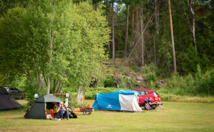 Två uppställda tält på en grön gräsmatta, i bakgrunden syns lummig skog.