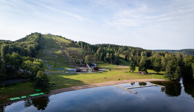 Vy ovanifrån på Flottsbros backe på sommaren, i förgrunden syns vattnet och himlen är blå.
