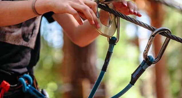 Bilden visar en närbild på en beskuren person iförd utrustning för Acropark i närbild syns händerna som håller linan.